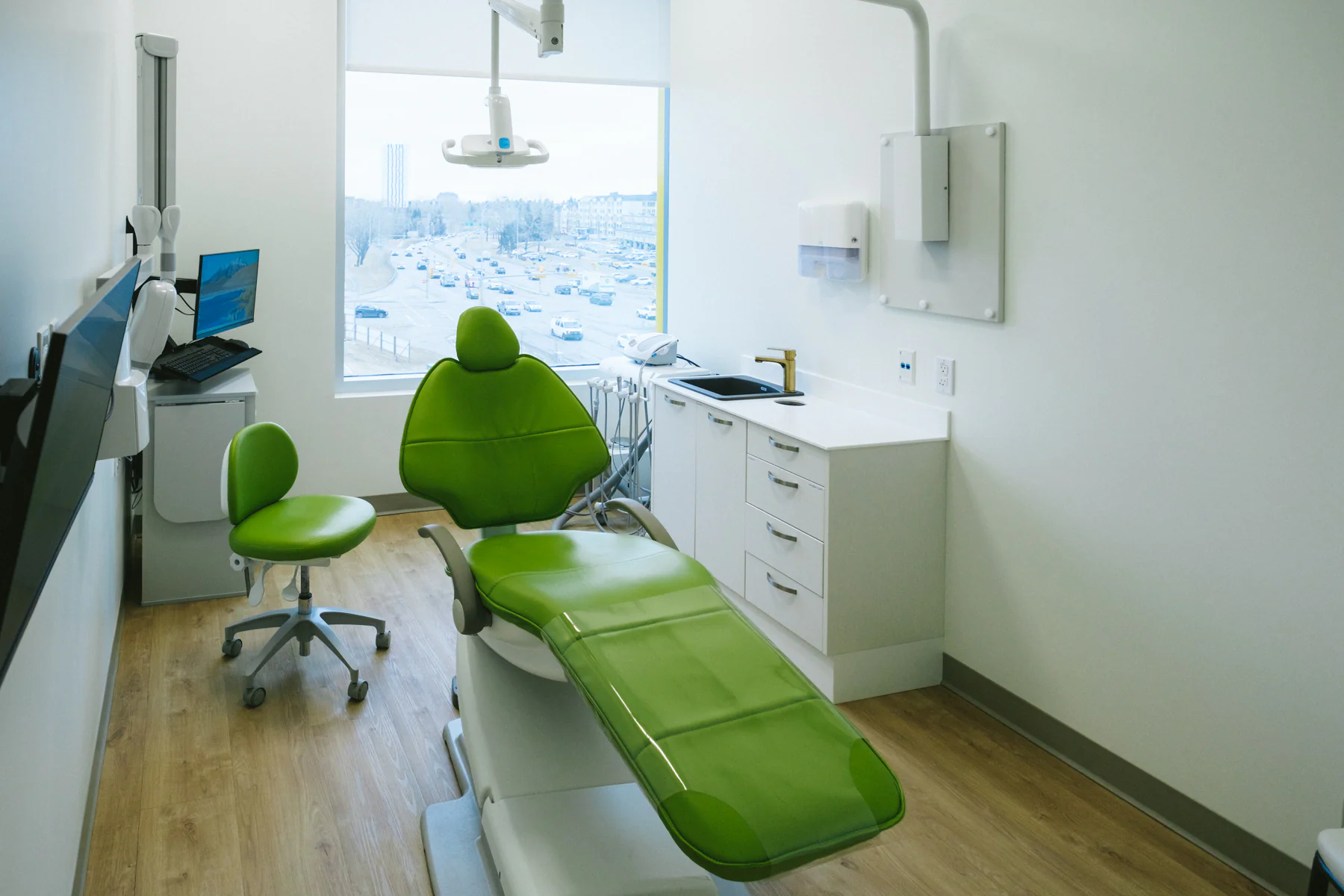 Bright treatment room with a green dental chair and neighbourhood window view