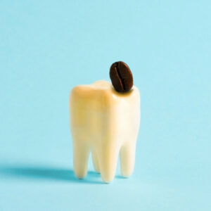 A model of a human tooth with yellow discoloration and a single coffee bean on top, set against a blue background.